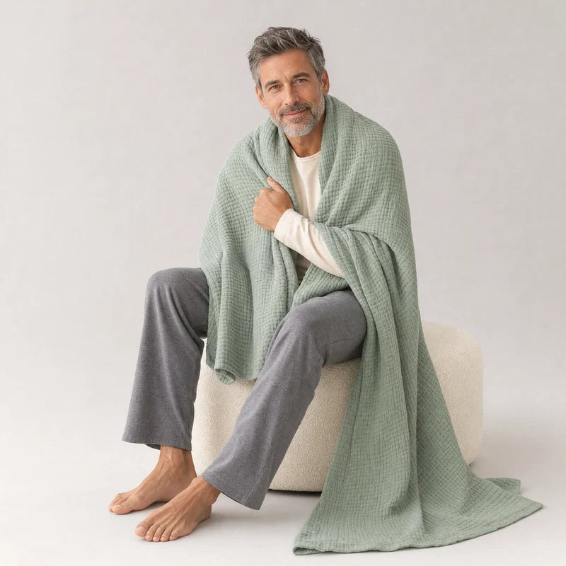 Man on a pouf with the Muslin Blanket in Green pooling on the floor